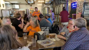 People gathering around a couple of tables at a craft brewery, some of them wearing bright orange Mobilize Waco T-shirts