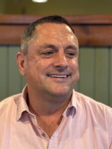 A white man wearing a collared shirt smiling for the camera